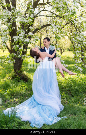 Braut und Bräutigam Mann zusammen halten und heben Sie seine Freundin. Junge Hochzeitspaar umfassend in blühenden Frühling Garten. Liebe und romantische Thema Stockfoto