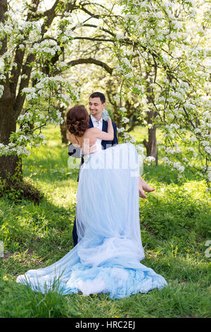 Braut und Bräutigam Mann zusammen halten und heben Sie seine Freundin. Junge Hochzeitspaar umfassend in blühenden Frühling Garten. Liebe und romantische Thema Stockfoto