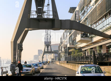 Hamburg, Deutschland - Februar 15, 2017: Historische Hafenkräne neben moderner Architektur auf der Uferpromenade in Altona. Menschen gehen durch. Stockfoto