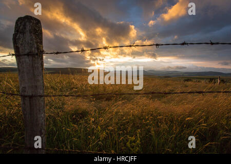 Alte rustikale Post und Stacheldraht Holzzaun und ein buntes Sonnenuntergang mit dramatische Wolken in der Auvergne, Frankreich in der Abenddämmerung Stockfoto