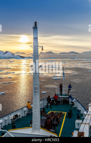 Menschen stehen auf den Schiffsbug beobachten den Sonnenuntergang unter Eisberge driften bei Lemaire-Kanal, Antarktis Stockfoto