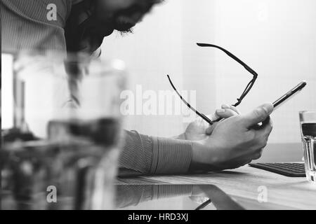 Geschäftsmann Hand mit mobilen Zahlungen online-shopping, Omnichannel, Laptop-Computer am Schreibtisch aus Holz, schwarz weiß Stockfoto