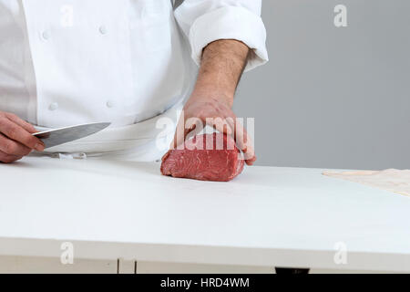 Nahaufnahme von den Händen von einem Metzger schneiden Scheiben von rohem Fleisch aus einem großen Lende für tournedos Stockfoto