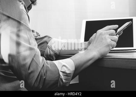 Erfolg Geschäftsmann Hand mit Brillen, Smartphone, Digital tablet Docking-smart-Tastatur auf Holz Schreibtisch, schwarz weiß Stockfoto