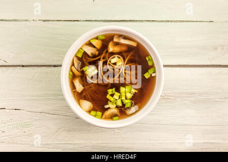 Ein Foto von einer Miso-Suppe mit Buchweizen Soba, Champignons und Frühlingszwiebeln, geschossen von oben auf eine hölzerne Hintergrundtextur mit Textfreiraum Stockfoto