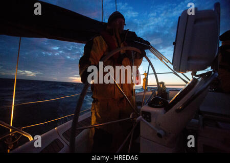 Reifer Mann Lenkrad auf Yacht im Meer bei Sonnenuntergang Stockfoto