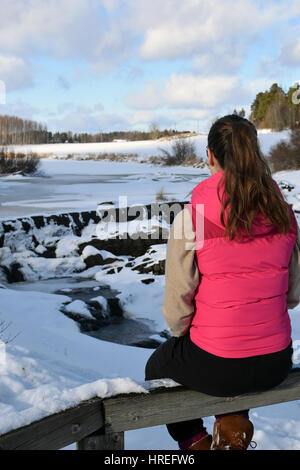 Teenager auf Zaun sitzen. Herrliche Winterlandschaft auf Hintergrund. Stockfoto