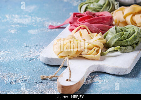 Verschiedene farbige frische rohe hausgemachte Teigwaren Tagliatelle grün Spinat, rosa rote Beete und traditionellen gelb auf weißem Holz schneiden Board ove Stockfoto