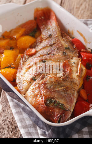 Tilapia-Fisch gebacken mit Paprika, Karotten und Thymian hautnah in Auflaufform auf den Tisch. vertikale Stockfoto