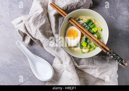 Weiße Schale mit asiatischen Stil Suppe mit Rührei, die Hälfte der marinierte Ei, Frühlingszwiebeln, Spinat serviert mit hölzernen Stäbchen, Löffel, Textile über gra Stockfoto