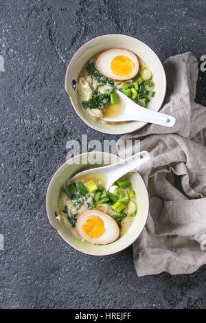 Zwei Schalen mit asiatischen Stil Suppe mit Rührei, die Hälfte der marinierte Ei, Frühlingszwiebeln, Spinat serviert mit weißen Löffel und Textil über schwarzer text Stockfoto