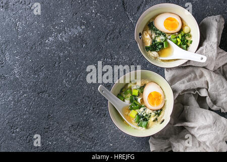 Zwei Schalen mit asiatischen Stil Suppe mit Rührei, die Hälfte der marinierte Ei, Frühlingszwiebeln, Spinat serviert mit weißen Löffel und Textil über schwarzer text Stockfoto