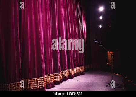 Bereit für Leistung, geschlossene Bühne mit großer dekorativer Vorhang, Mikrofon am Stand vor der es groß und Lampen und Leuchten in Ecke. Stockfoto