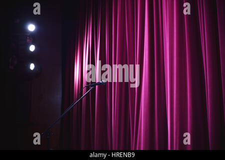 Bereit für Leistung, geschlossene Bühne mit großer dekorativer Vorhang, Mikrofon am Stand vor der es groß und Lampen und Leuchten in Ecke. Stockfoto