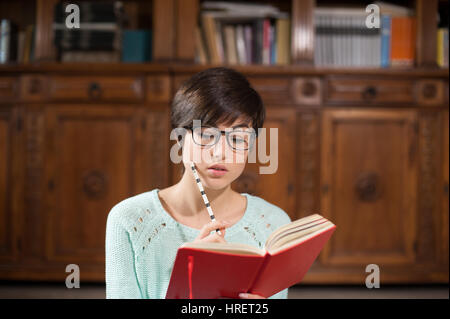 Junge Studentin aufschreiben auf Notizblock mit großen Bücherregal im Hintergrund Stockfoto