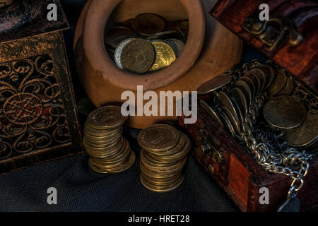 Schatztruhe, Stapel und Säule der Münzen, eine Keramikschale voller Schmuck Münzen und Kerze Lampe in dunkler Umgebung Stockfoto