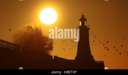 Wellen über die Mole-Mauer bei Tynemouth Leuchtturm in North Shields als die Sonne steigt am ersten Tag des meteorologischen Frühlings. Stockfoto