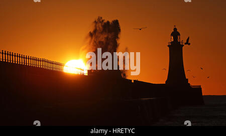 Wellen über die Mole-Mauer bei Tynemouth Leuchtturm in North Shields als die Sonne steigt am ersten Tag des meteorologischen Frühlings. Stockfoto