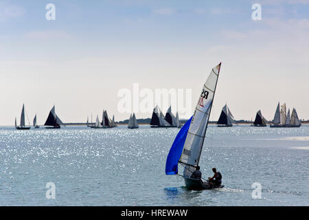 kleine Jolle Segeln in Richtung einer Regatta mit einer Flotte von Yachten und Segelboote in der Ferne am Horizont Stockfoto