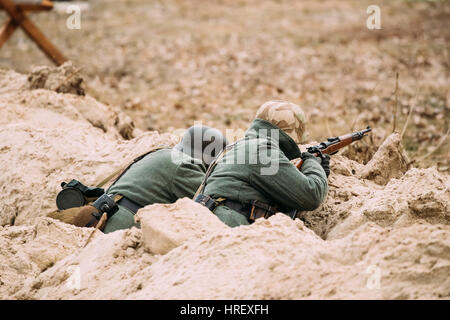 Zwei nicht identifizierte Reenactor verkleidet als deutsche Wehrmacht Infanterie Soldaten im zweiten Weltkrieg versteckt sitzen mit Gewehr In einen Hinterhalt im Graben In Waffe Stockfoto