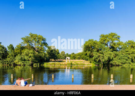 LONDON - Juli 19: Paar sitzt an einem See im Hyde Park mit den Füßen im Wasser an einem heißen sonnigen Tag am 19. Juli 2016 in London Stockfoto