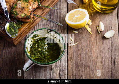 Hausgemachtes Chimichurri Sauce in ländlichen weiße Tasse auf rustikalen Holztisch, traditionellen Marinade oder Sauce zu gegrilltem Fleisch Stockfoto