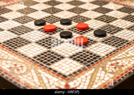 Rote und schwarze Checker Stücke auf einem Mosaik Stein Spieltisch. Stockfoto