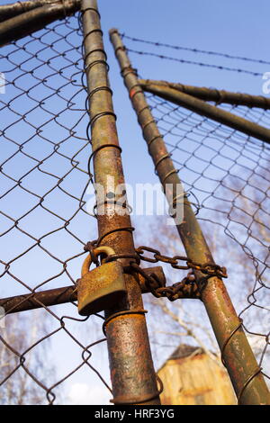 Rostige Vintage metallischen Vorhängeschloss hängt an alte Maschendraht Tor Stockfoto