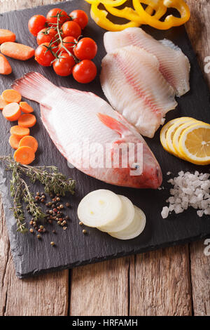 Rohe frische rote Tilapia und Gemüse, Gewürze-close-up auf dem Tisch. vertikale Stockfoto