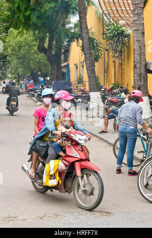 Einen lokalen vietnamesischen Familie Mutter und ihre Kinder in Hoi an Masken eine alte Stadt, Reiten, einen Motorroller oder Moped Gesicht tragen aber keine Helmpflicht. Stockfoto