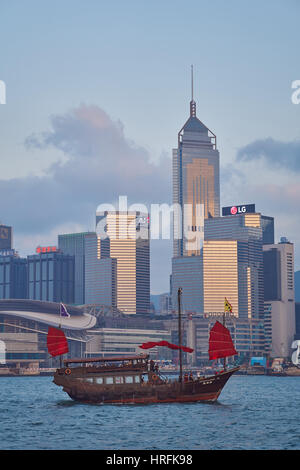 Blick von Kowloon auf das traditionelle rote Segel einer chinesischen Dschunke und über den Hafen auf die Hong Kong Skyline im Hintergrund - Hongkong, China Stockfoto