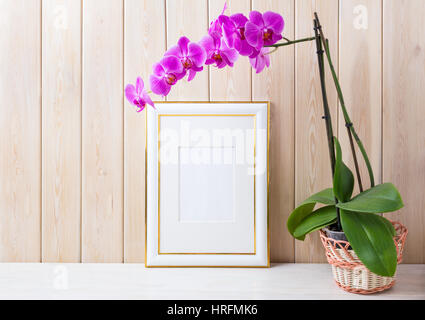 Verzierte Goldrahmen Mockup mit Magenta-lila Orchidee im Weidenkorb in der Nähe von Holzwand. Leere Rahmen mock up für Präsentationsdesign.  Rustikale Rahmung Stockfoto