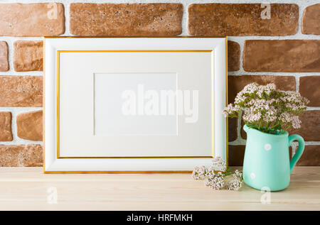 Gold geschmückten Landschaft Frame Modell mit wilden sehr weich rosa Blumen in Vase in der Nähe von Backstein-Mauer. Leere Rahmen mock up für Präsentationsdesign. Stockfoto