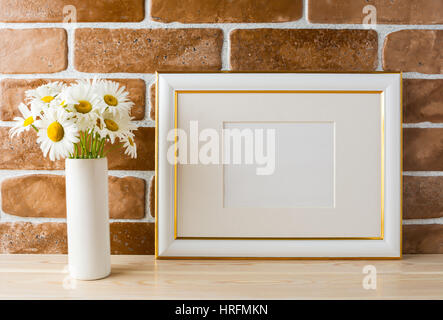 Gold geschmückten Landschaft Frame Modell mit Daisy Bouquet in gestaltete Vase in der Nähe von Backstein-Mauer. Leere Rahmen mock up für Präsentationsdesign.  Templat Stockfoto