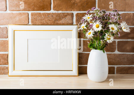 Gold geschmückten Landschaft Frame Modell mit Wildblumen Blumenstrauß in gestaltete Vase in der Nähe von Backstein-Mauer. Leere Rahmen mock up für Präsentationsdesign.  T Stockfoto