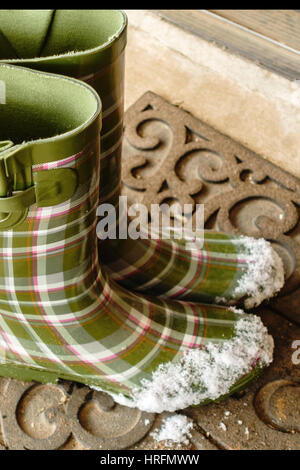 Grüne Damen Gummistiefel oder Gummistiefel, mit Schnee auf den Zehen gemustert. Ruht auf eine willkommene Matte. Stockfoto