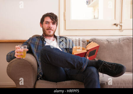 Junger Mann in seinem Wohnzimmer mit einem karierten Hemd und ein Buch Stockfoto