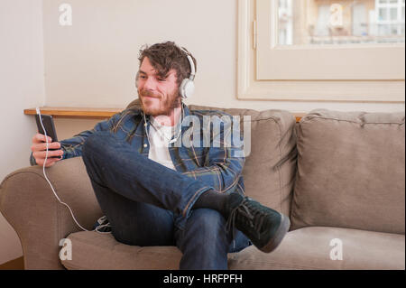 Junger Mann in seinem Wohnzimmer mit einem karierten Hemd, Musik hören Stockfoto