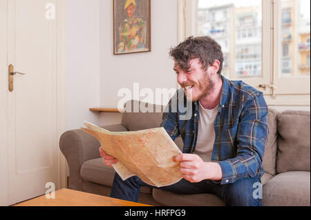 Junger Mann in seinem Wohnzimmer mit einem karierten Hemd und einer Karte Stockfoto