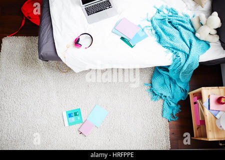 Draufsicht der Teen Zimmer mit Laptop, Decke hängend nach unten vom Bett und Schule Bücher liegen auf Teppich Stockfoto