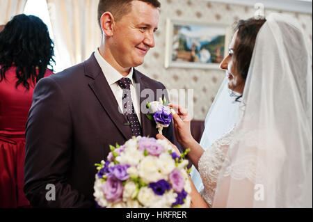 Braut eingeflößt Knopfloch in Jacke Bräutigam am Hochzeitstag am ersten treffen. Stockfoto