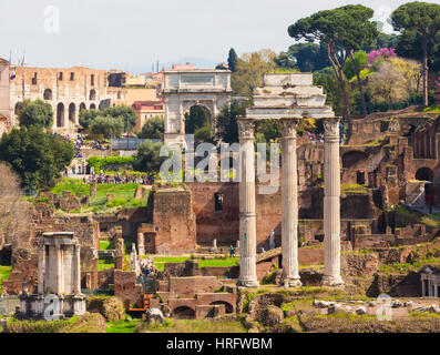 Rom, Italien.  Das Forum Romanum. Die drei Säulen der Tempel des Castor und Pollux.  Der Titus-Bogen im Hintergrund. Das Forum ist Teil des Hi Stockfoto