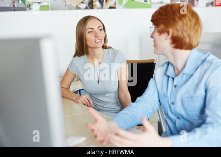 Attraktive junge Geschäftsfrau mit langen blonden Haaren Projekt Diskussion mit ihrem männlichen Kollegen beim Sitzen im Großraumbüro Stockfoto
