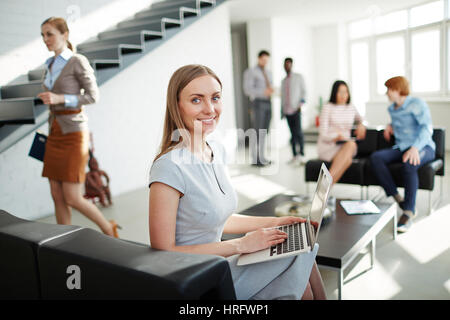 Portrait von junge hübsche Geschäftsfrau auf bequemen Sessel im Büro Lobby sitzen und arbeiten zum Finanzbericht mit Hilfe von laptop Stockfoto