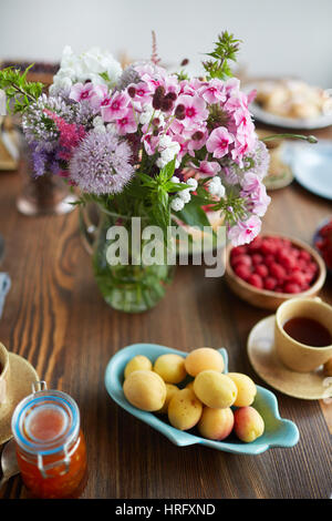 Stillleben mit frisch geschnittenem Wiesenblumen in Vase, Reife Aprikosen und Himbeeren aus dem Garten und Tasse Tee auf dunklen Holztisch gelegt Stockfoto