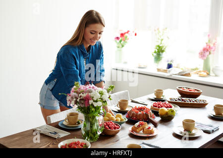 Junge hübsche Frau Tisch mit köstlichen hausgemachten Desserts, Garten Obst und Beeren, Feldblumen und Teetassen Stockfoto