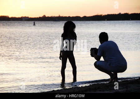 Fotograf nimmt Bilder eines Modells bei Sonnenuntergang auf dem Meer Miami Skyline bei Sonnenuntergang, von Key Biscayne Stockfoto