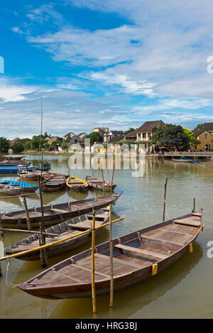 Eine Ansicht Inl Hoi an eine alte Stadt mit hölzernen Touristen- und Angelboote/Fischerboote am Thu Bon Fluss neben der Cau An Hoi an Brücke an einem sonnigen Tag mit blauem Himmel. Stockfoto