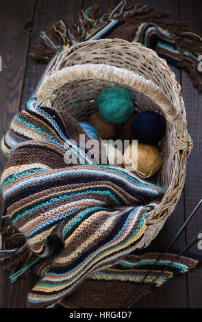 Gestrickte Wolle Schal und Garn Kugeln in einem Weidenkorb auf eine Holzoberfläche Stockfoto