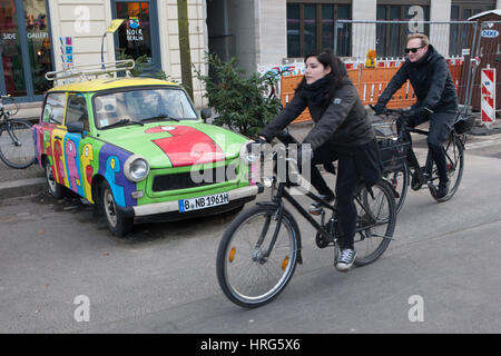 Radfahrer passieren die Trabant, gemalt vom französischen Künstler Thierry Noir in Berlin, Deutschland. Stockfoto